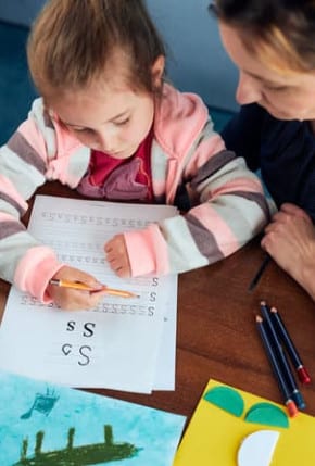 Enfant qui fait ses devoirs accompagnée d'un adulte